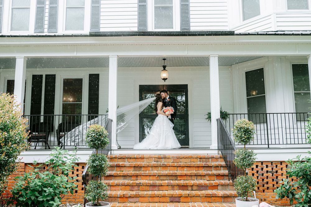 Bride and groom share a romantic kiss on the brick steps of a charming white Southern farmhouse wedding venue.