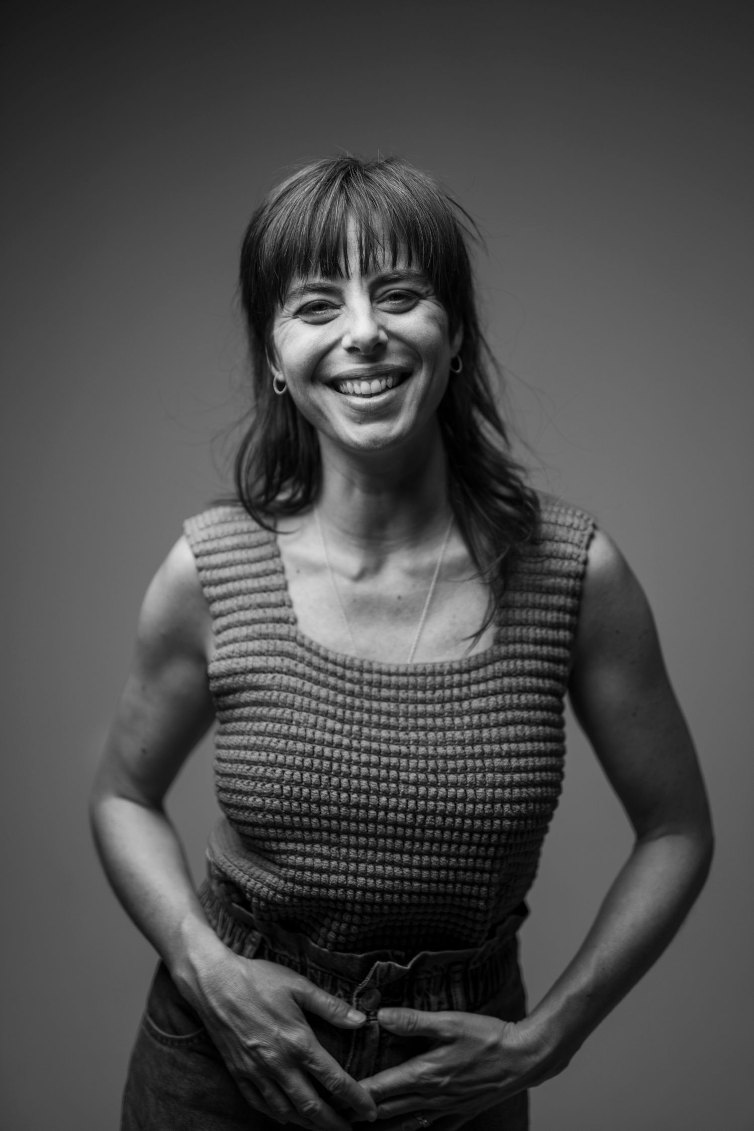 Black and white portrait of a smiling woman with bangs wearing a knitted sleeveless top.