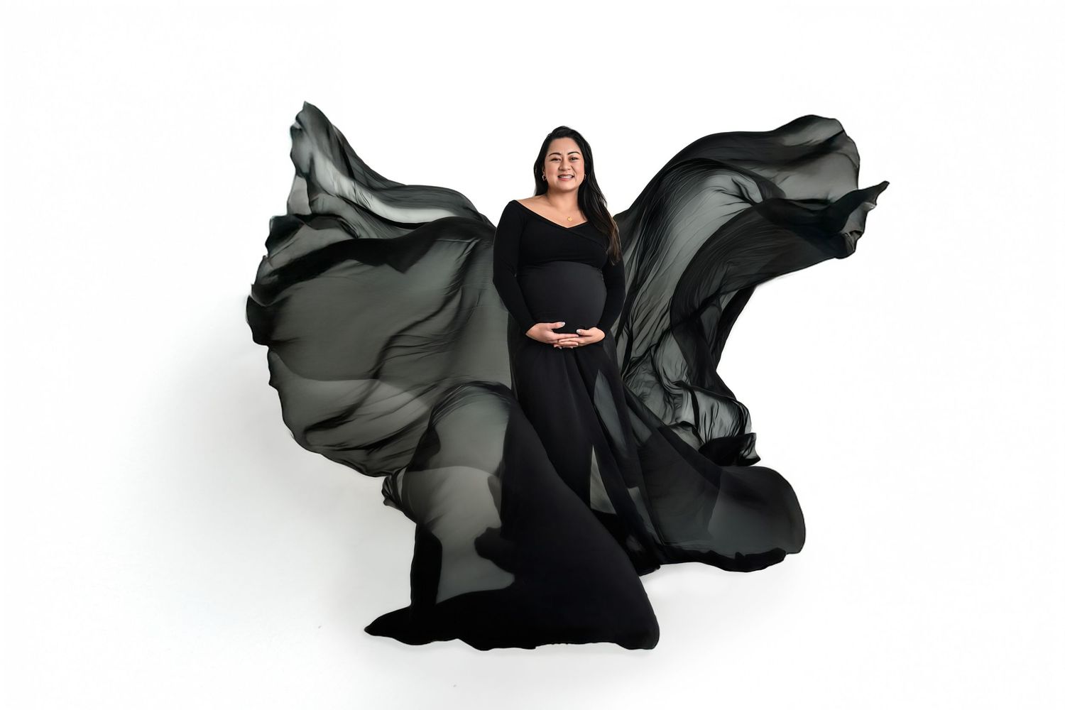 Pregnant woman in flowing black maternity gown with dramatic fabric movement on white backdrop for studio maternity photos in Marietta.