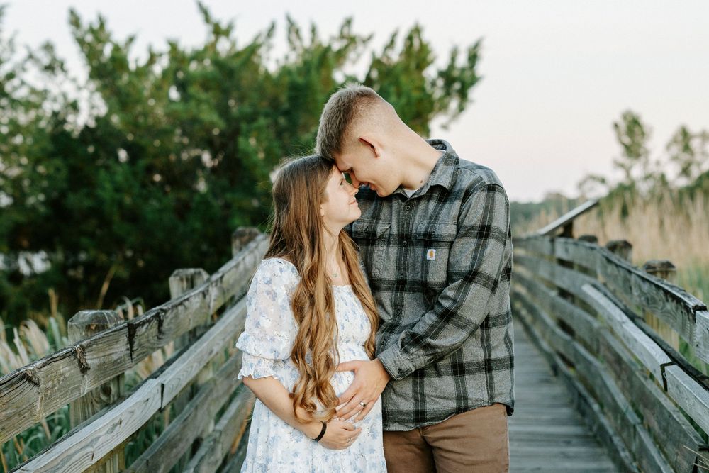 Couple sharing a romantic moment on a wooden bridge surrounded by lush greenery during golden hour.