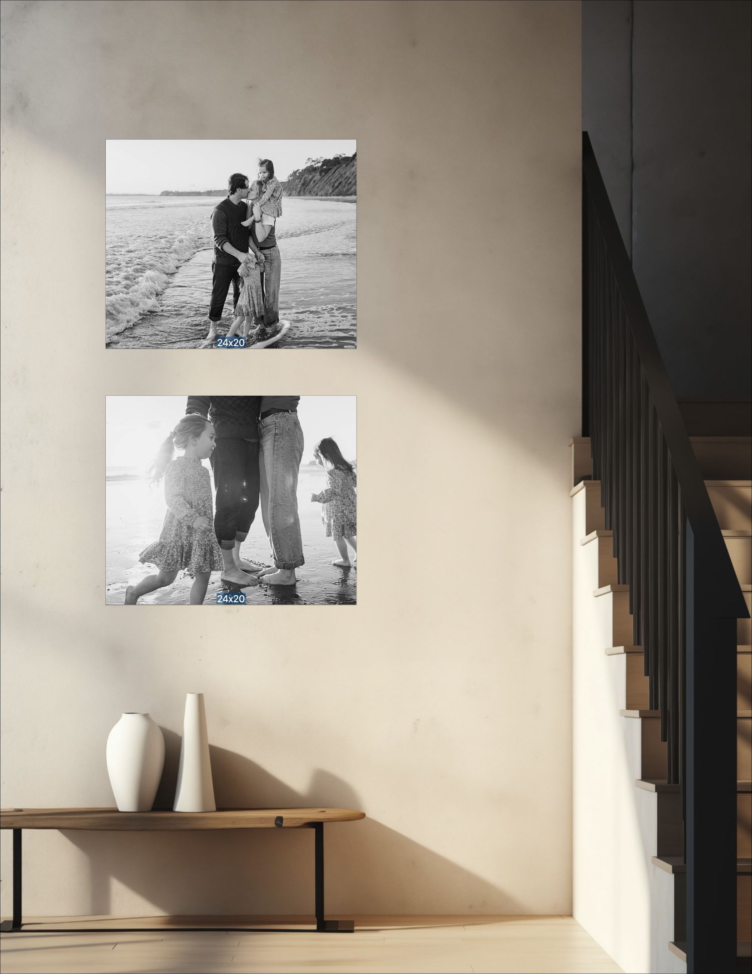 Black and white photo display of two beach family portraits hung on a neutral wall above a wooden bench with white vases.