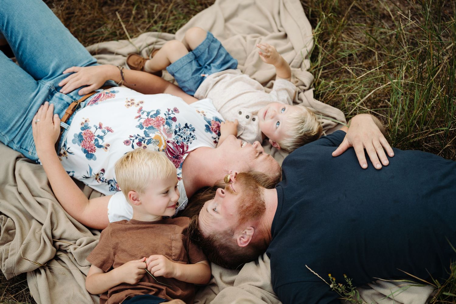 Family lying on a blanket in a field, parents and young children cuddling together outdoors in a storytelling photography session