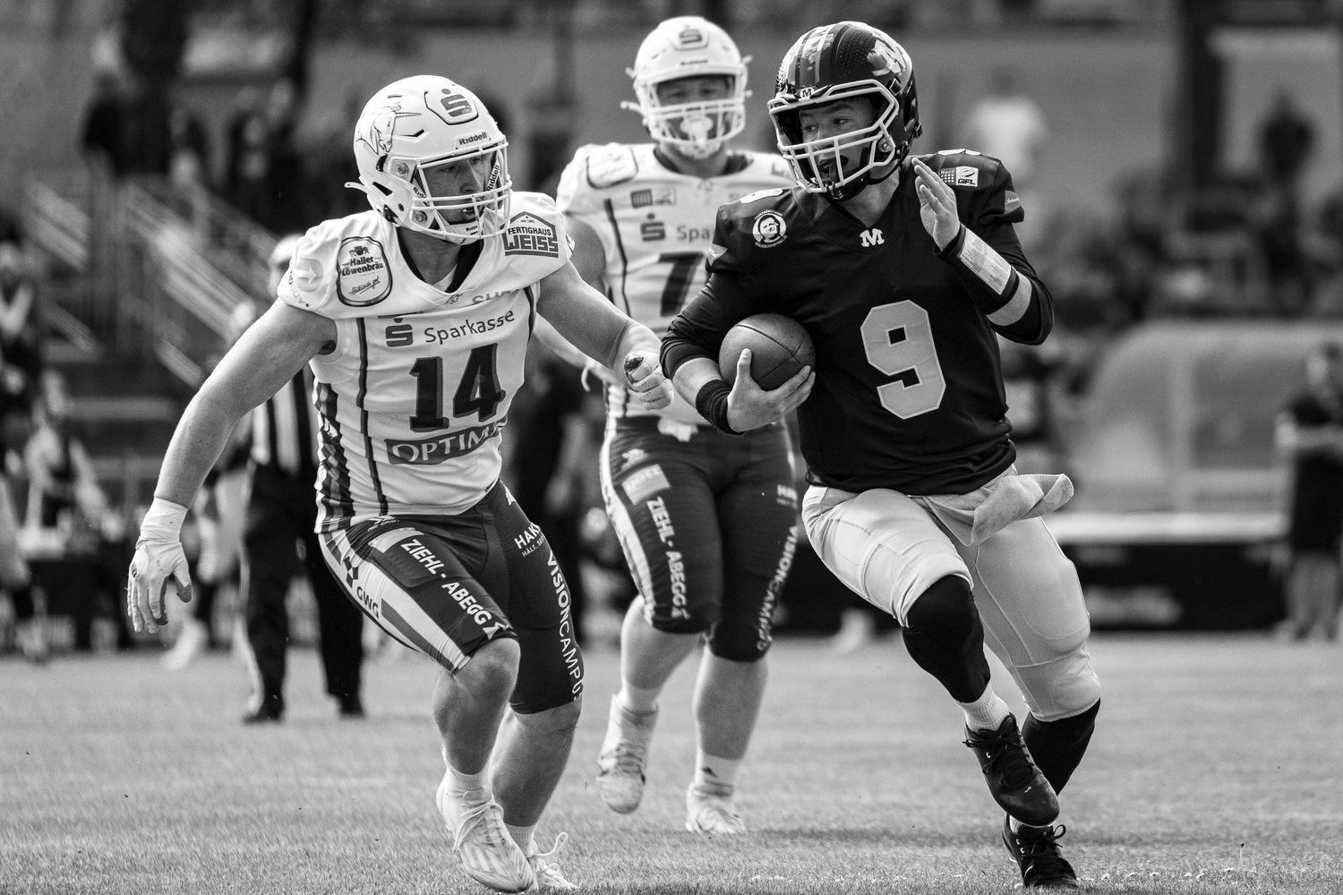 Black and white photo of football player number 9 running with the ball during a competitive game.