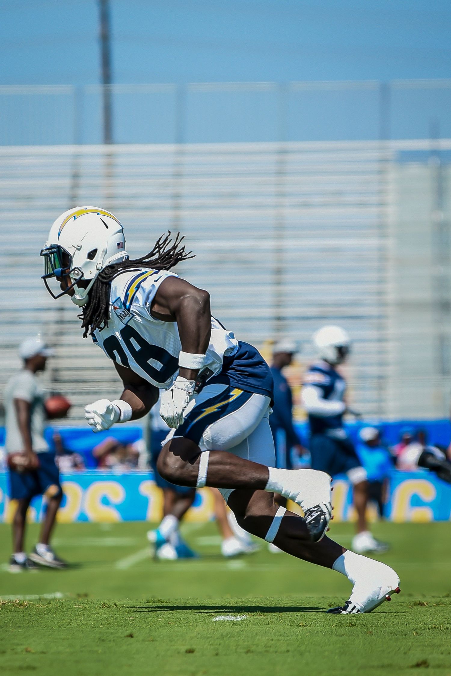 Football player in white Chargers uniform sprinting forward during a practice session.