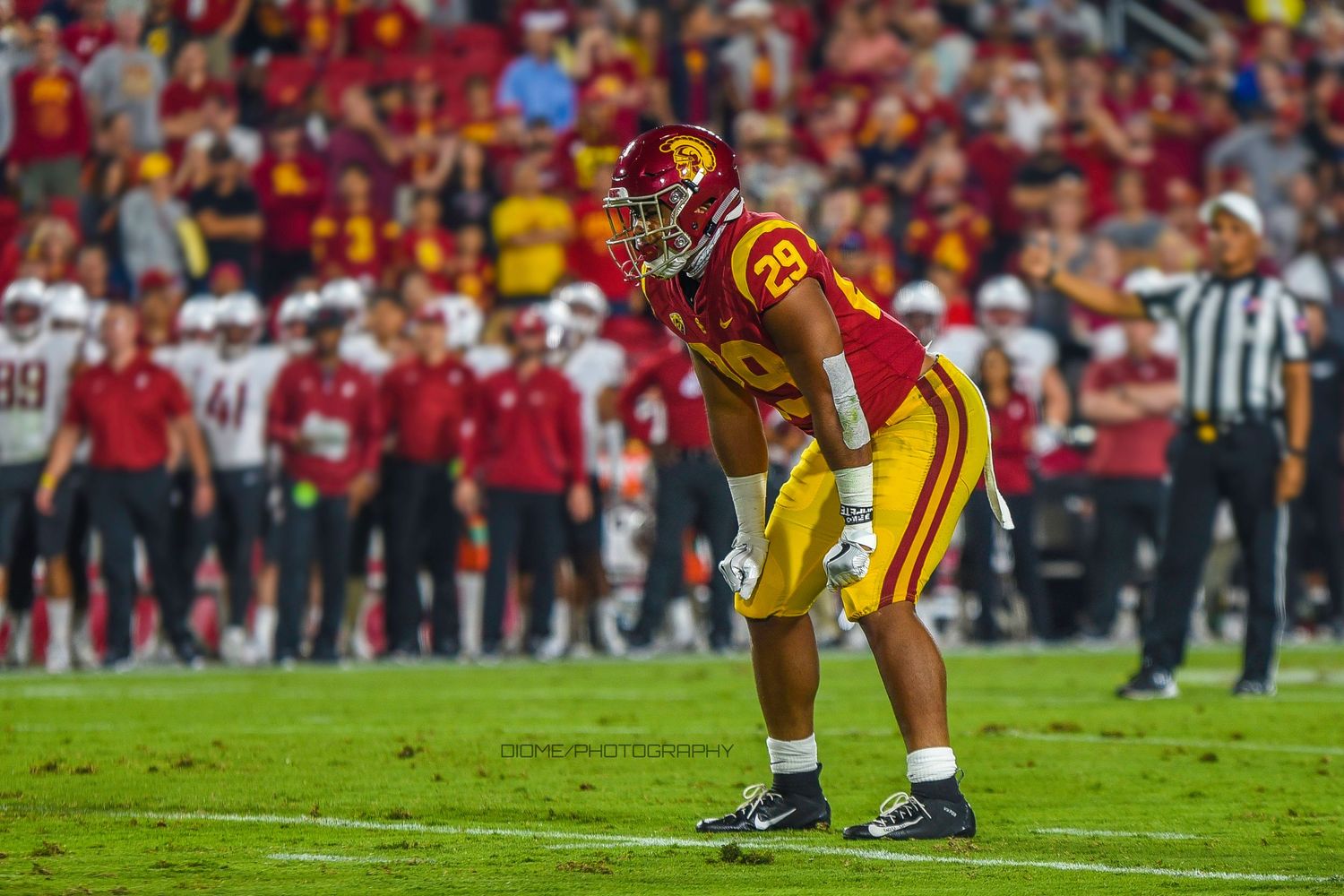 Football player in USC cardinal and gold uniform in defensive stance on field.