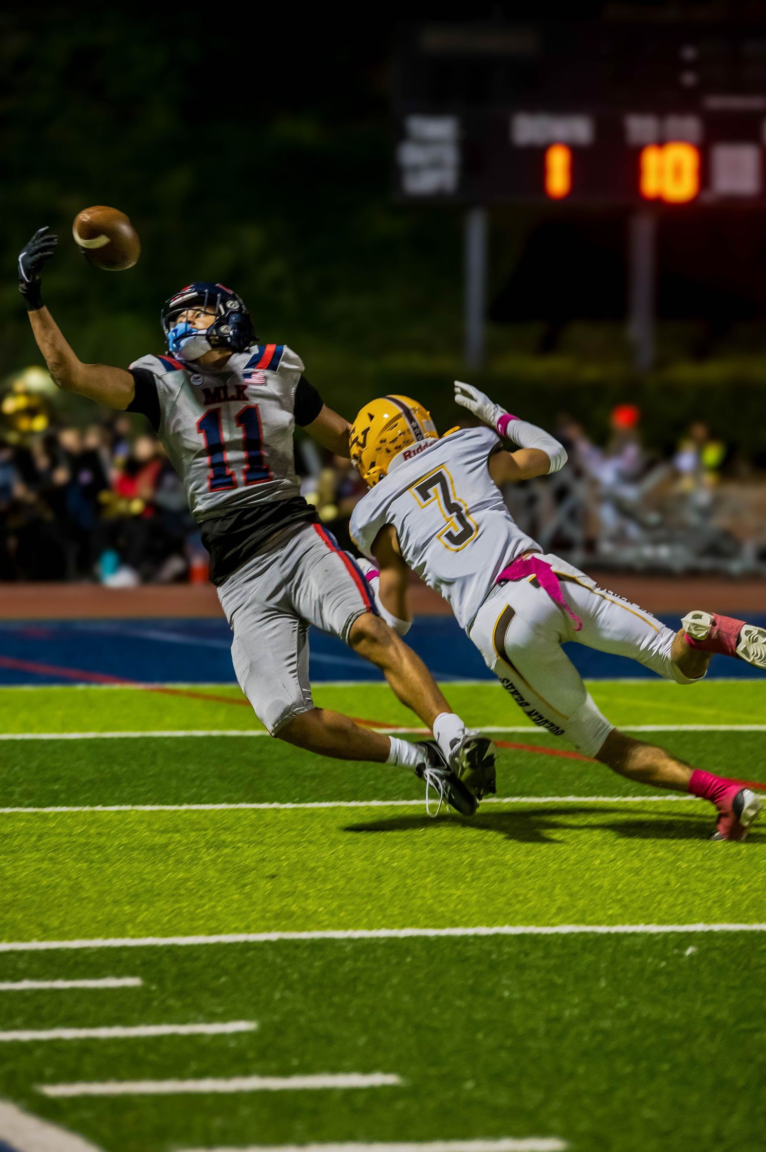 Two football players diving for the ball during a dramatic play under stadium lights.