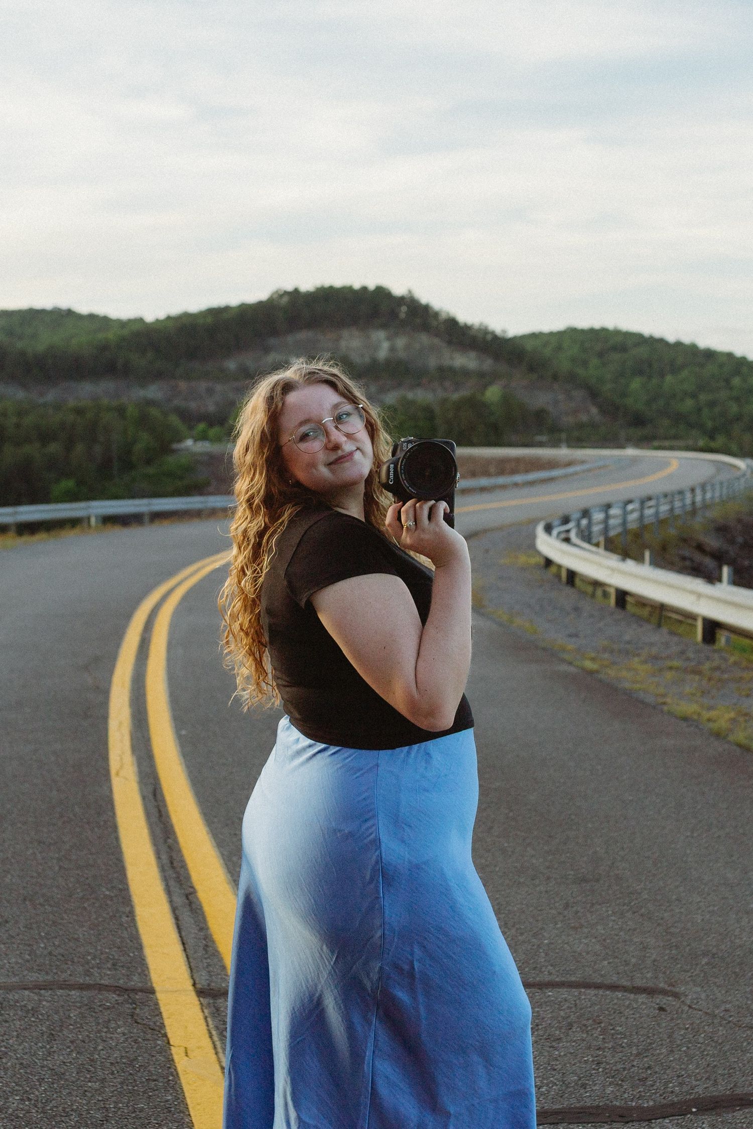Intimate wedding and elopement photographer Sydney Shepherd stands in the middle of an empty road with her camera