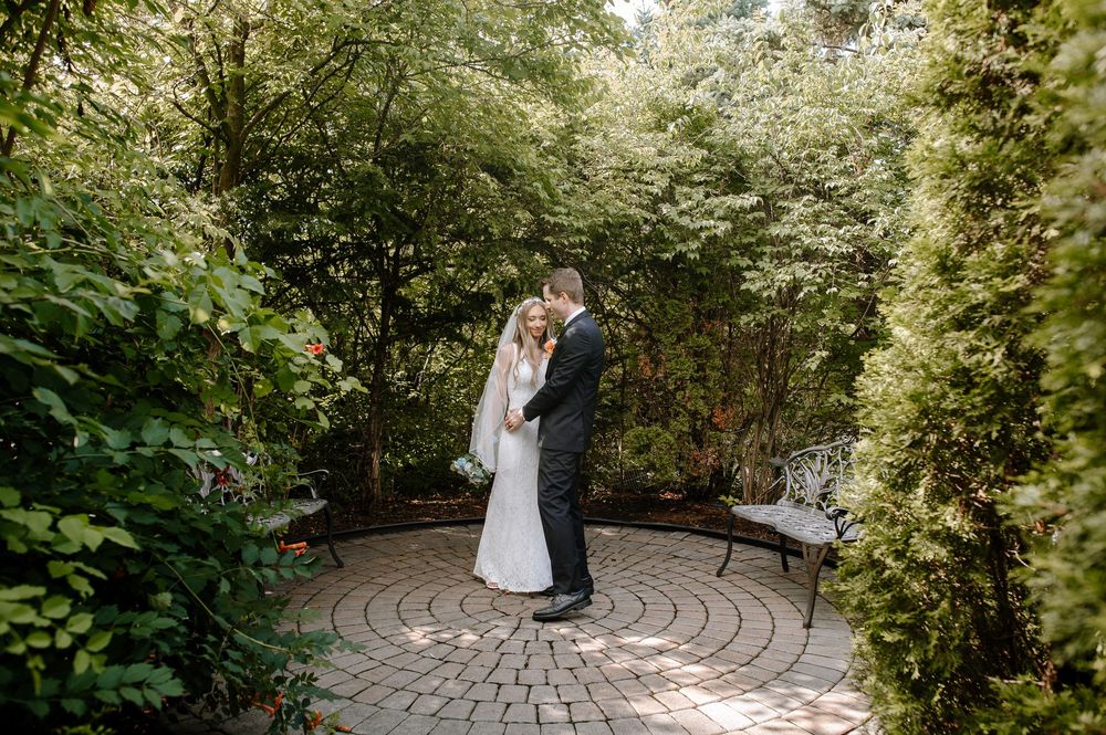 A couple shares an intimate moment on a circular stone patio surrounded by lush garden greenery and flowering bushes.