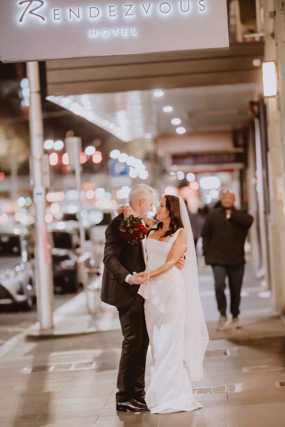 A couple shares their first dance under twinkling lights outside Rendezvous Hotel during a romantic wedding celebration.