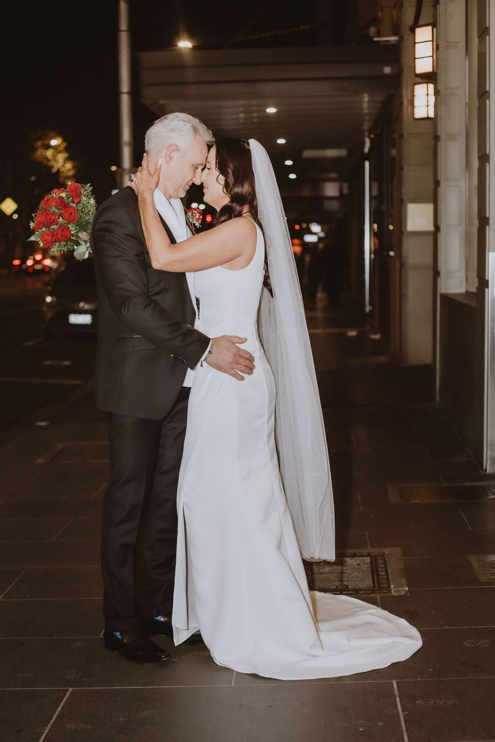 A bride and groom share an intimate embrace in a dimly lit parking garage during their wedding celebration.