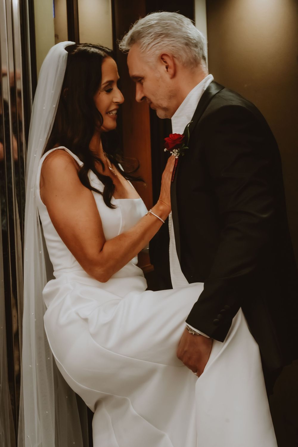 Intimate wedding moment between bride in white gown and groom in dark suit sharing tender embrace in hallway.