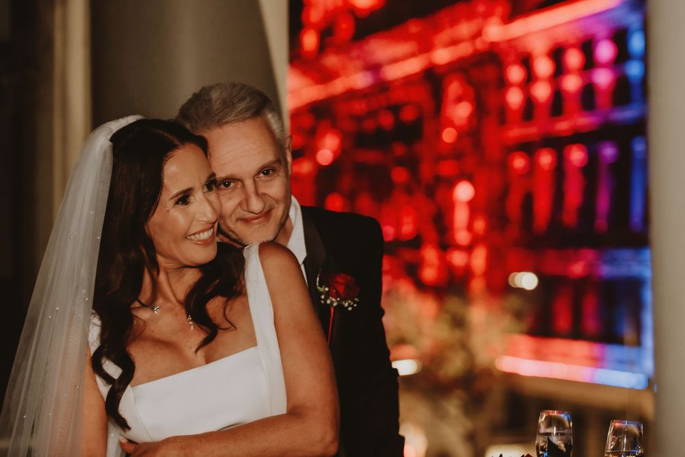 Newlyweds share an intimate moment together at an evening reception with glowing red lights in the background.
