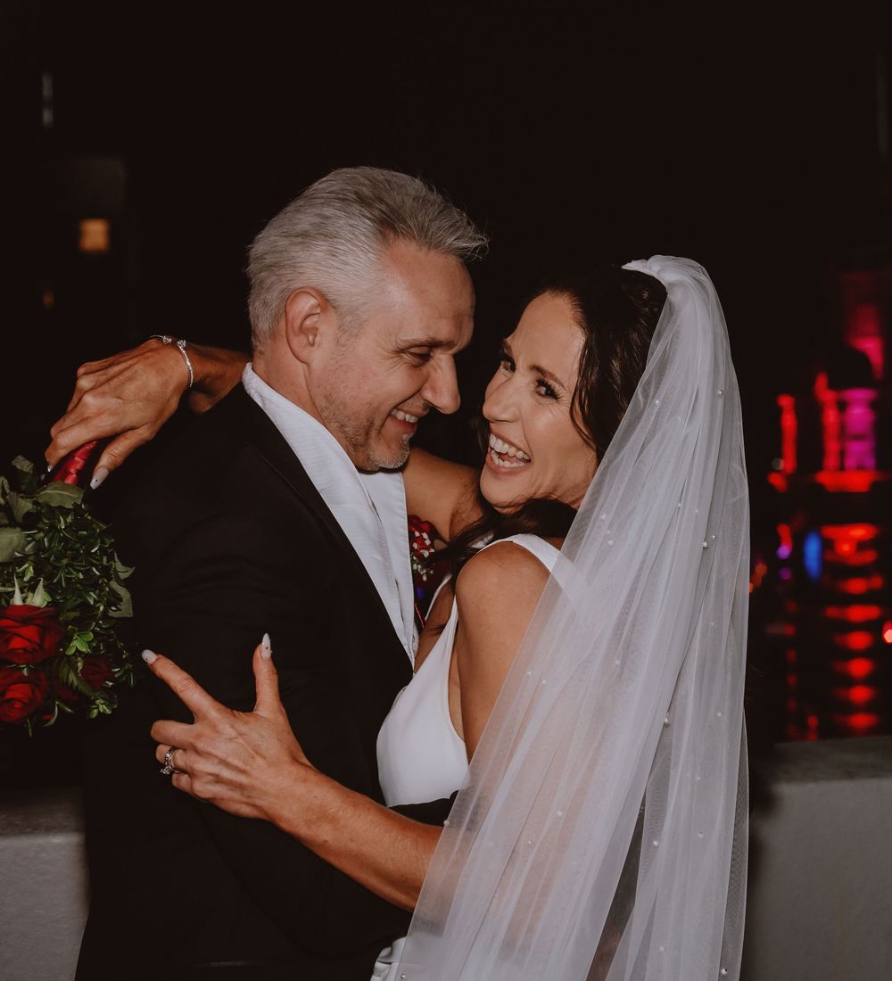 Intimate wedding moment captured against dark backdrop with red neon lighting.