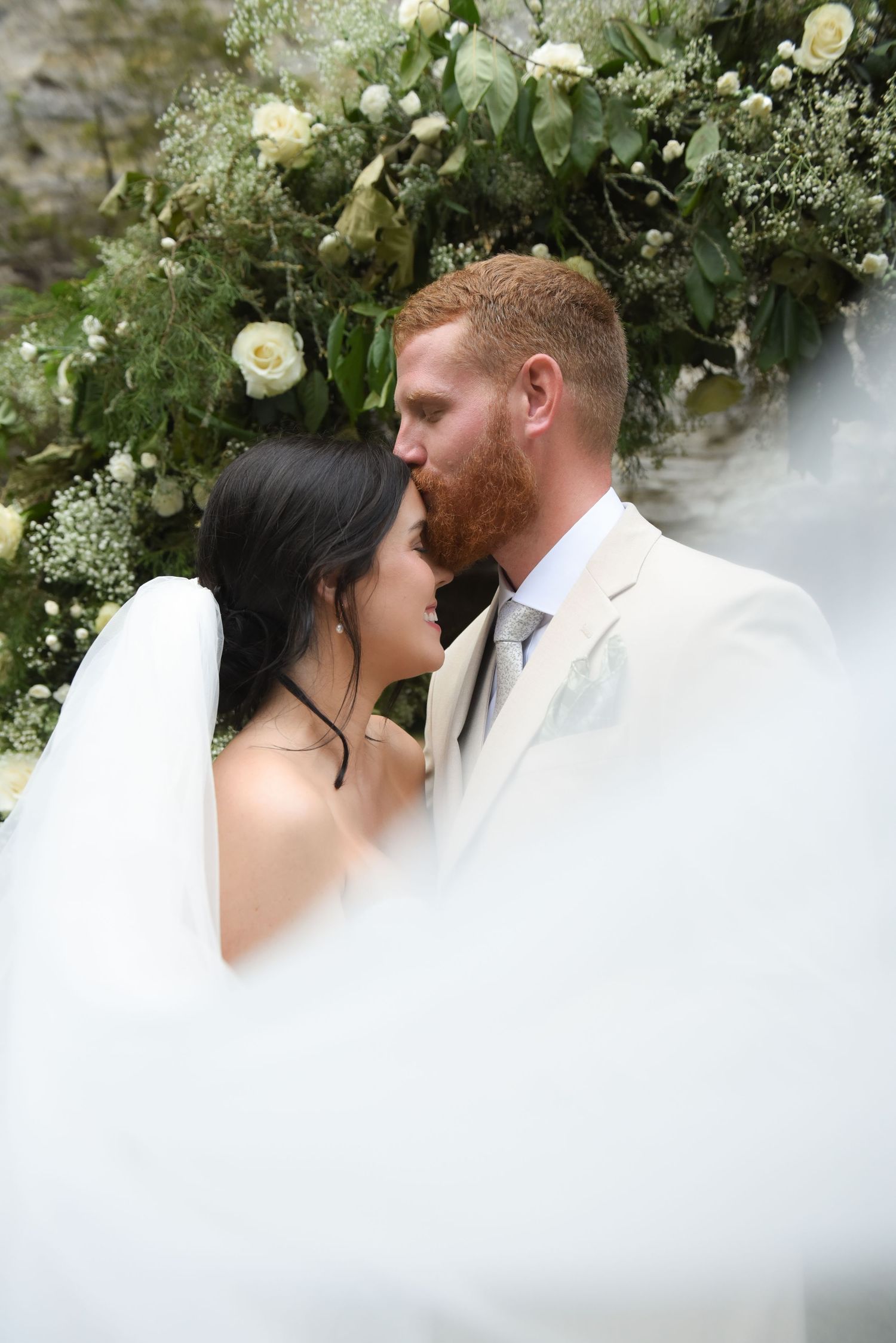 Intimate wedding moment framed by white roses and greenery arrangements.
