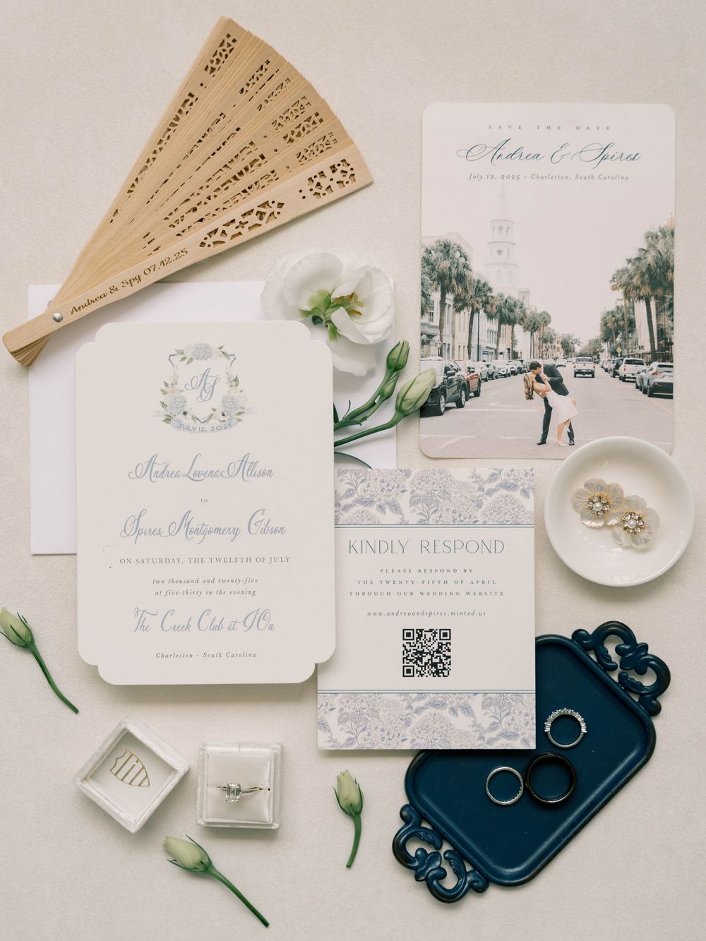 Elegant wedding stationery flat lay with invitations, rings and decorative elements on white background.