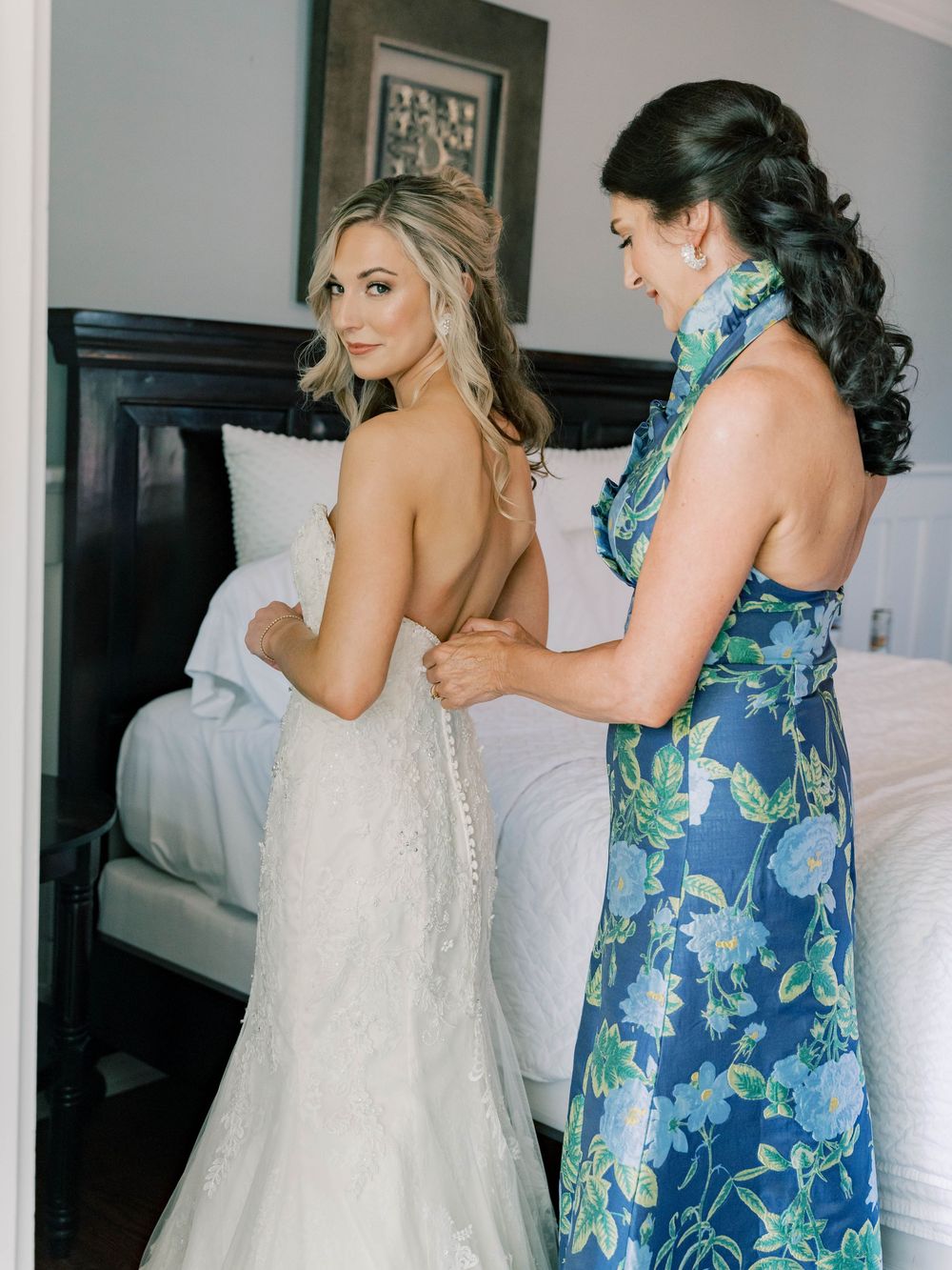 Wedding preparations showing bridesmaids in floral blue dresses helping with the bride's gown.