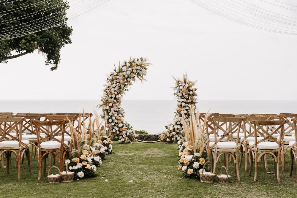Rustic outdoor wedding ceremony setup with wooden chairs and floral arrangements against a scenic backdrop.