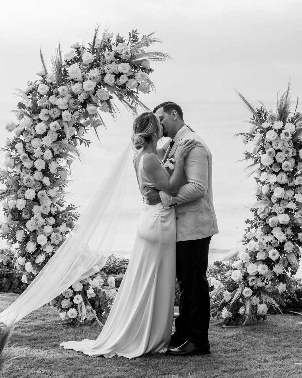 Black and white romantic wedding photography series showing a couple embracing beside floral arrangements.