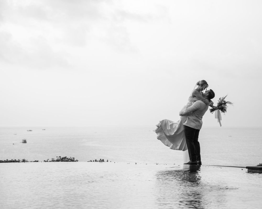 A couple embraces while wading into calm ocean waters creating a romantic silhouette against gray clouds.