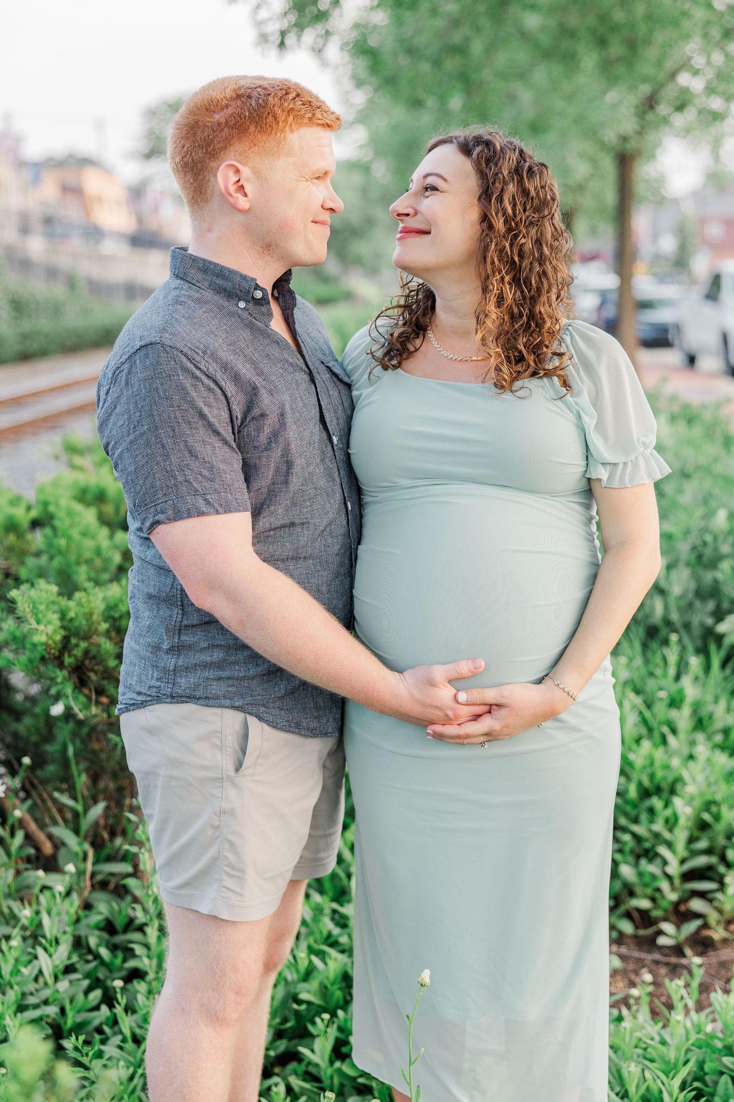 A couple shares intimate moments during their maternity photoshoot in a garden setting.