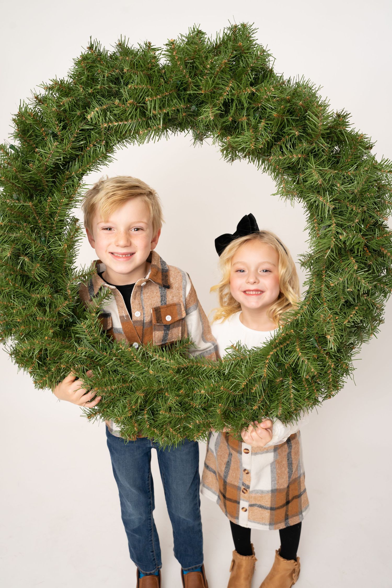 Children peek playfully through holiday wreath in creative photo series.