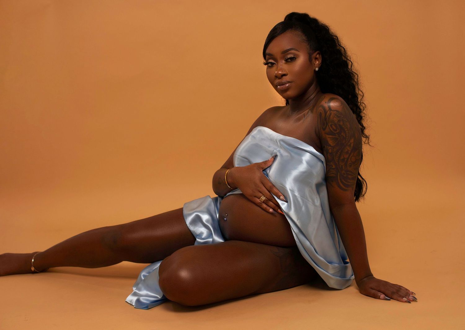 A figure in a light blue silk robe poses gracefully on a rust-colored backdrop in a contemporary studio setting.