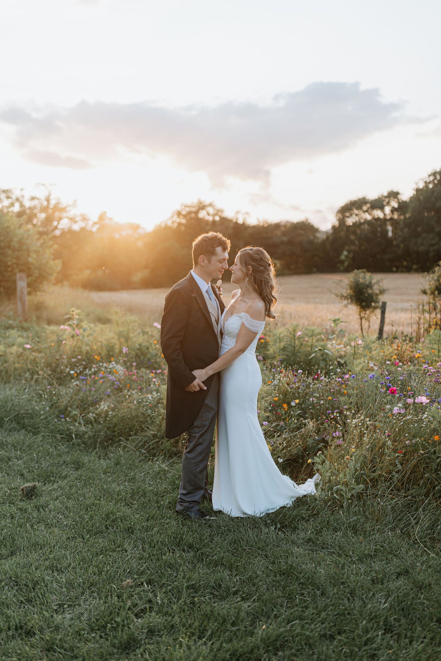 A couple shares an intimate moment at sunset in a wildflower meadow wearing formal wedding attire.
