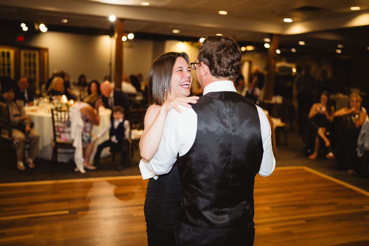 A couple shares an intimate dance moment during a wedding reception on a wooden dance floor.