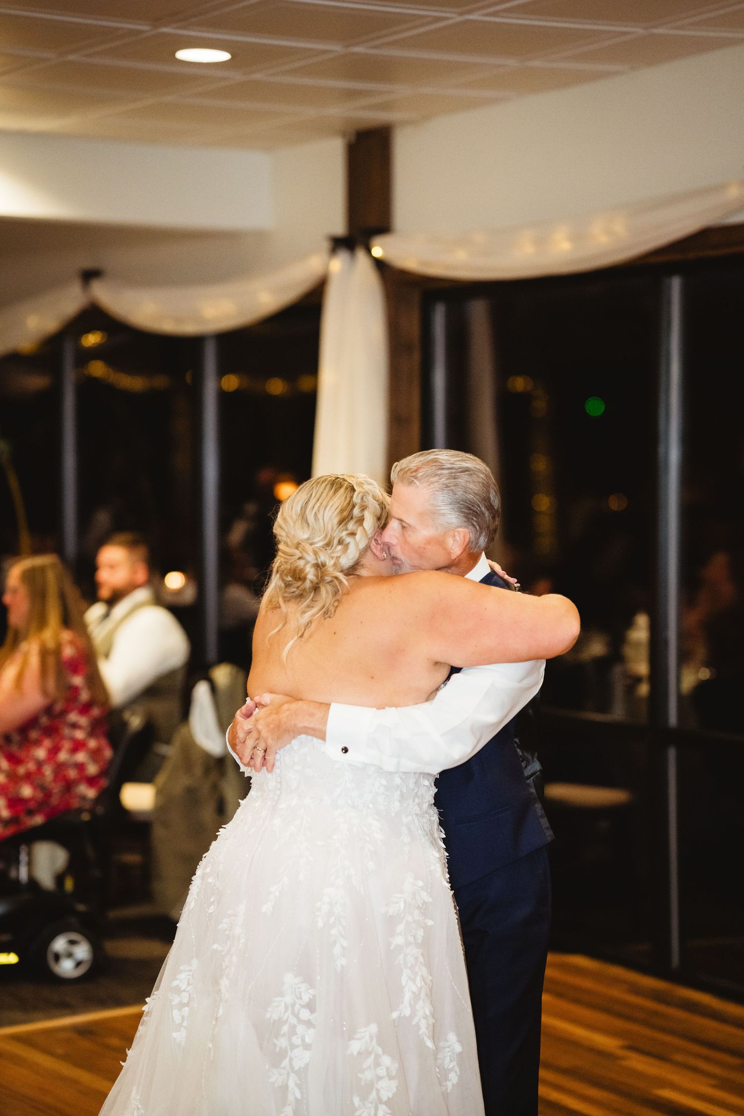 A tender dance moment at a wedding reception with an elegant white dress and decorative drapes in the background.