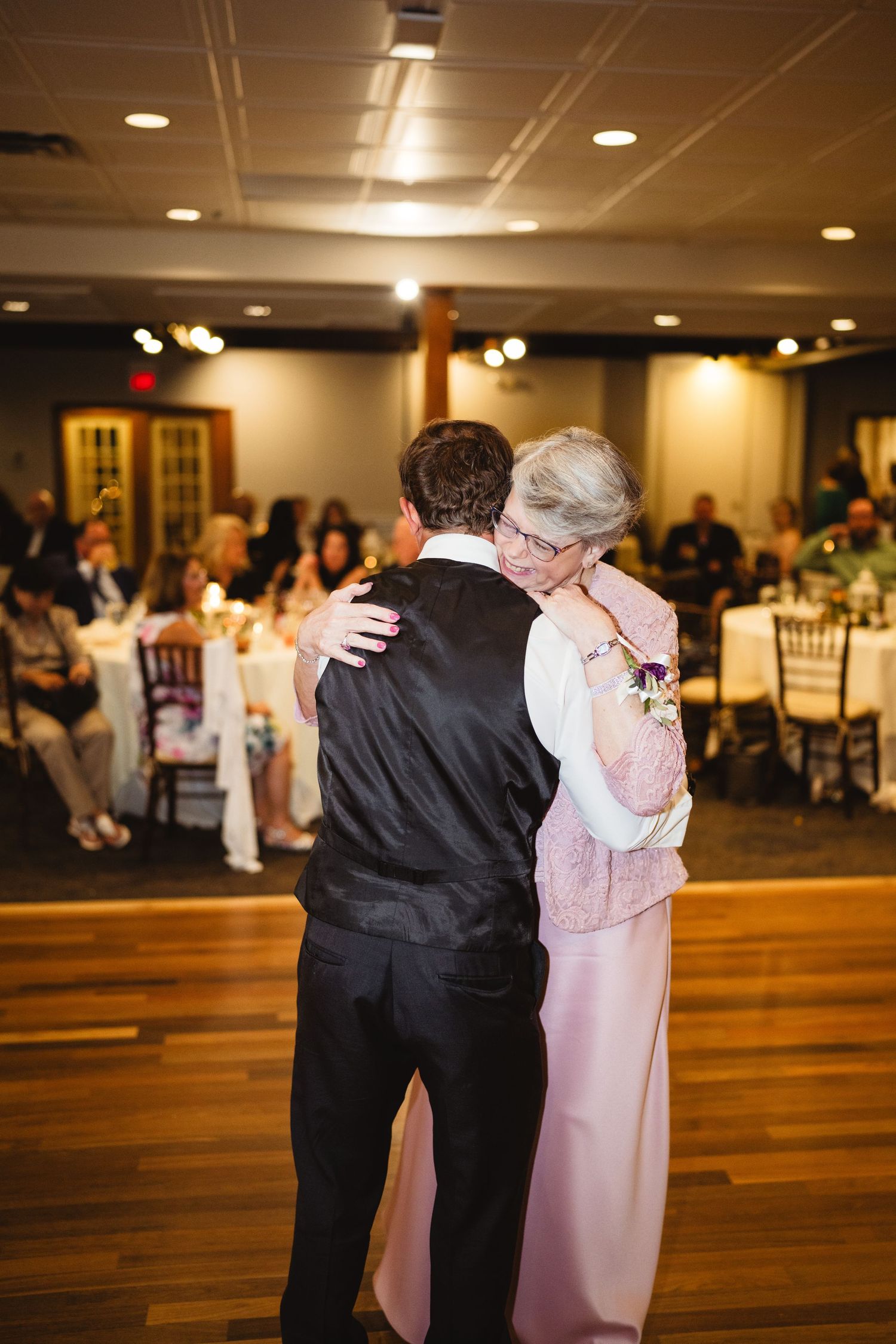 Couples dance together on a wooden floor at an elegant indoor venue with warm lighting.