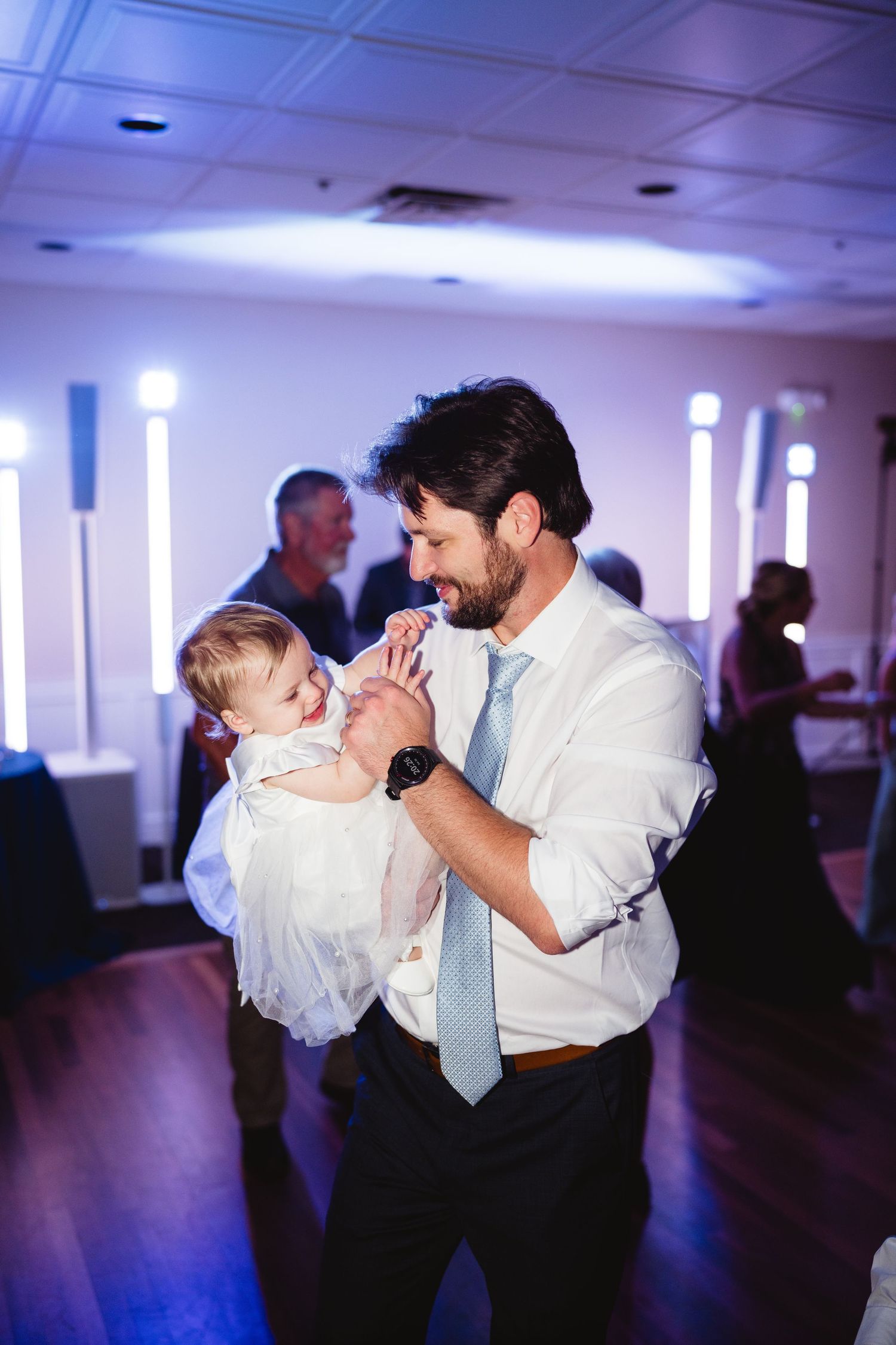 A touching moment on the dance floor as a baby in white is held during a wedding celebration.