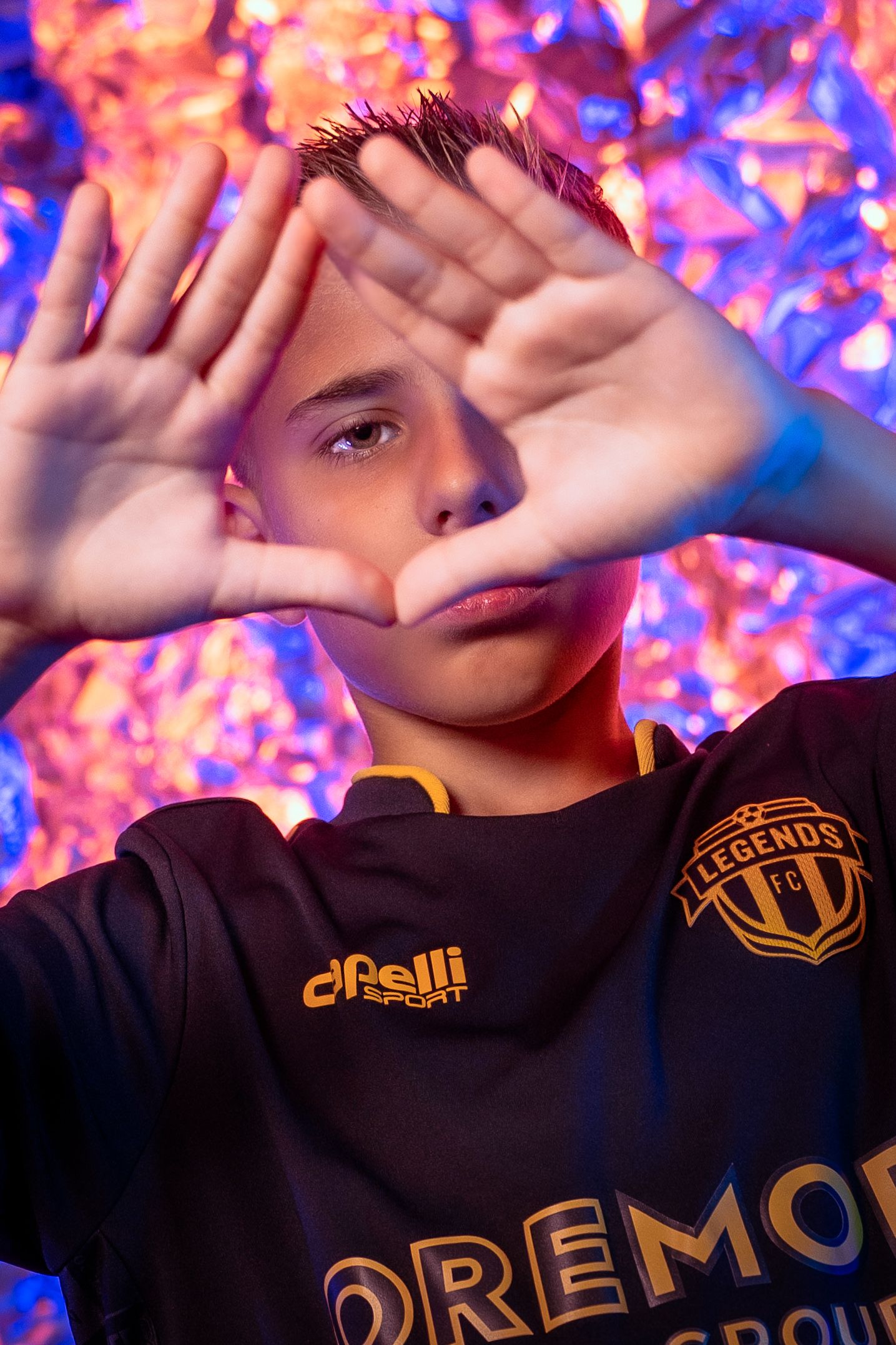 Youth in sports jersey poses against colorful pink and blue bokeh background.