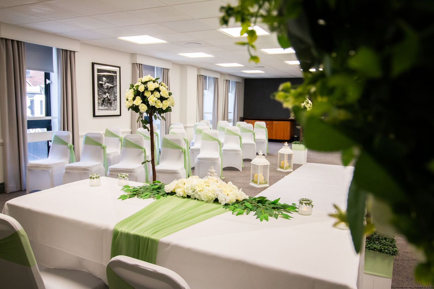 Clean modern event space with white chairs and green floral decorations.
