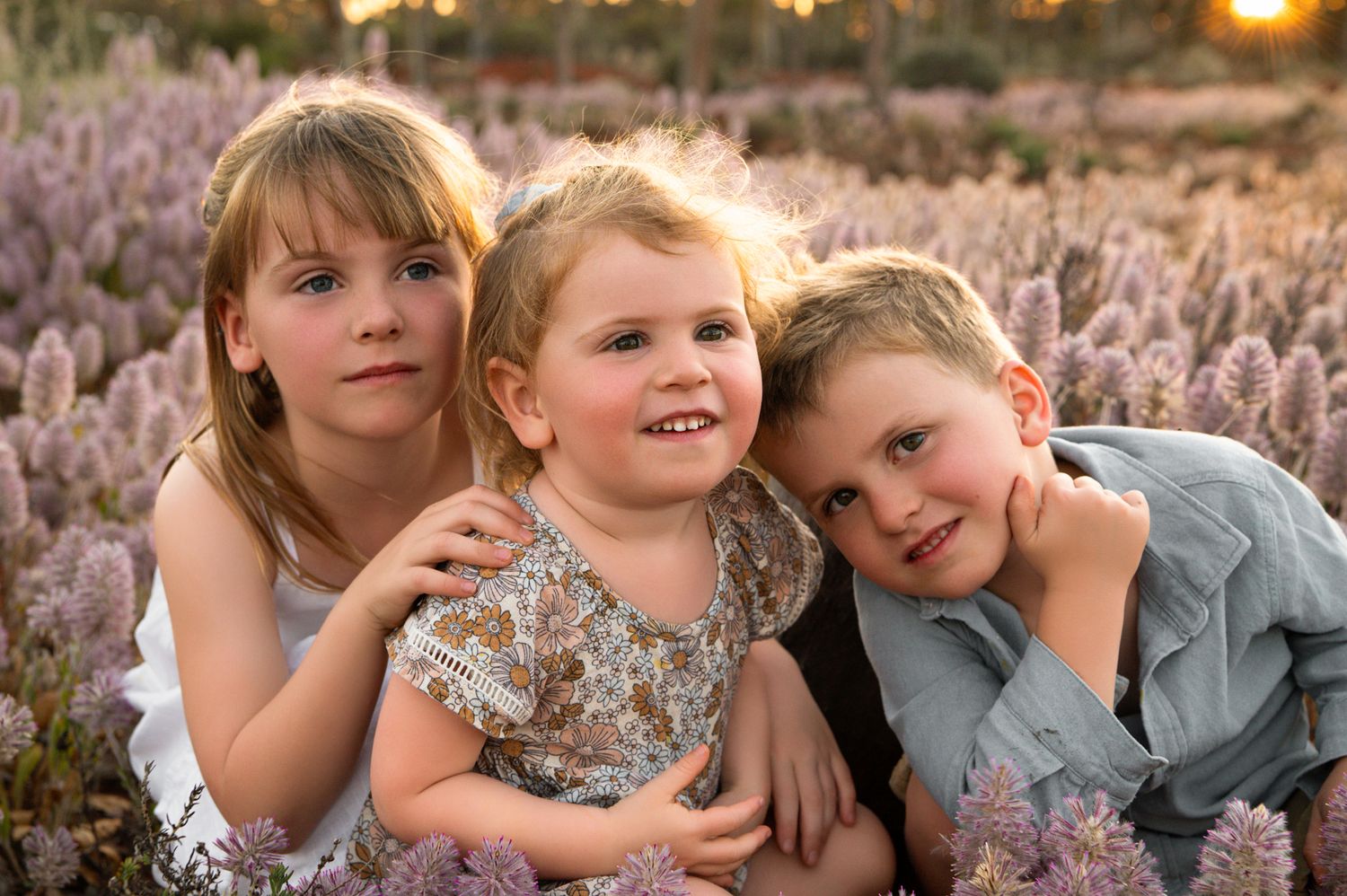 Children sit together and smile in a field of lavender flowers at sunset.