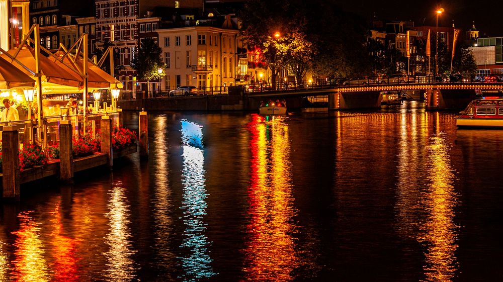 Urban waterfront at night with buildings casting warm light reflections across dark water.
