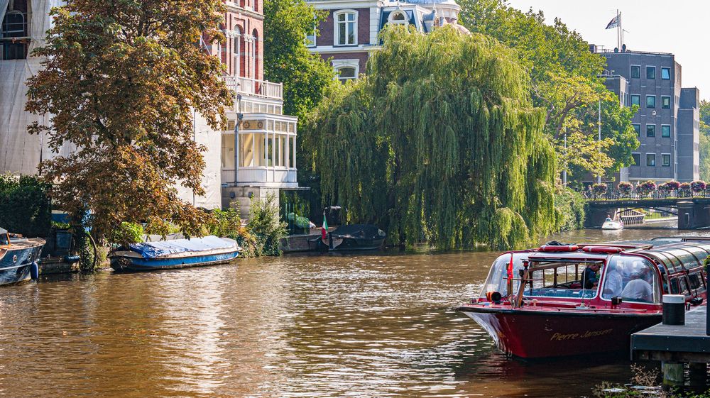 Canal lined with traditional Dutch buildings and boats under autumn trees.