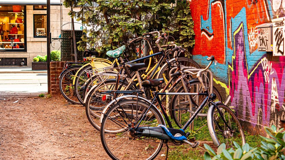 Row of colorful bikes parked against graffiti covered wall in urban setting.