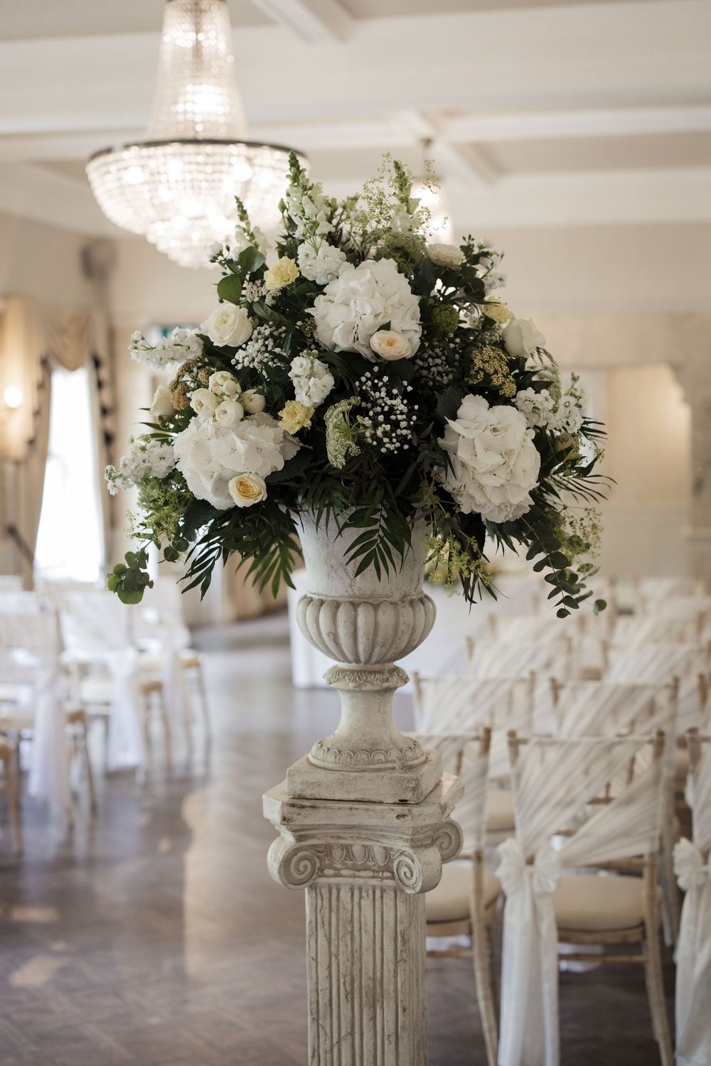 White floral arrangements on classical pillars line an elegant wedding venue interior.