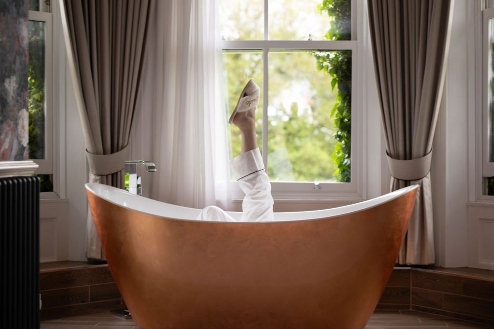 Luxurious freestanding copper bathtub positioned by window with brown curtains.