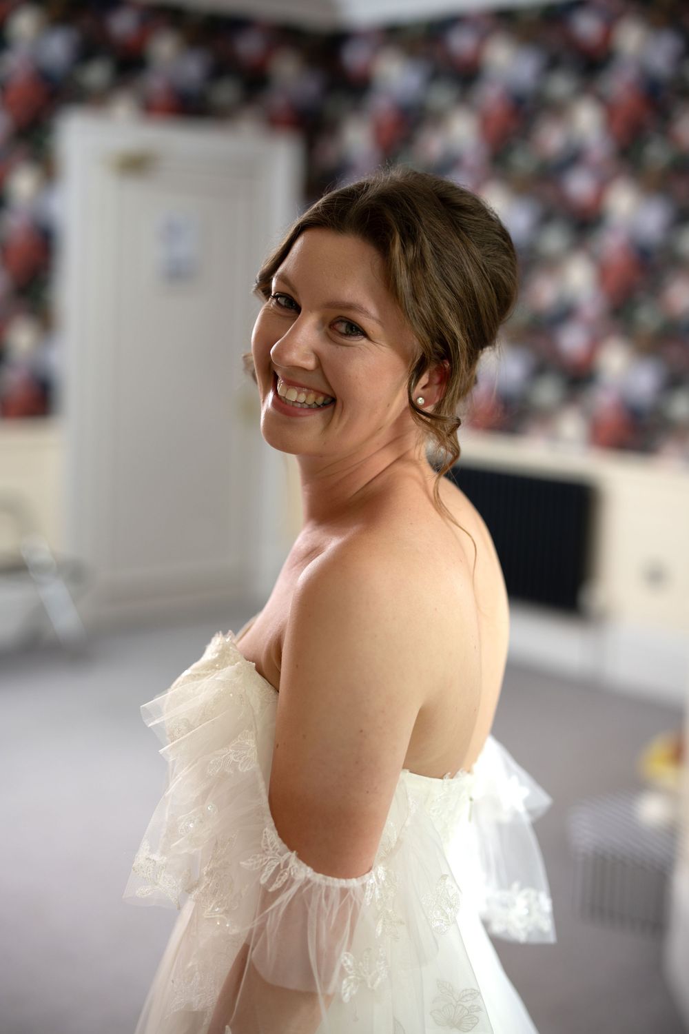 An elegant bride in a white off-shoulder wedding dress smiling joyfully.