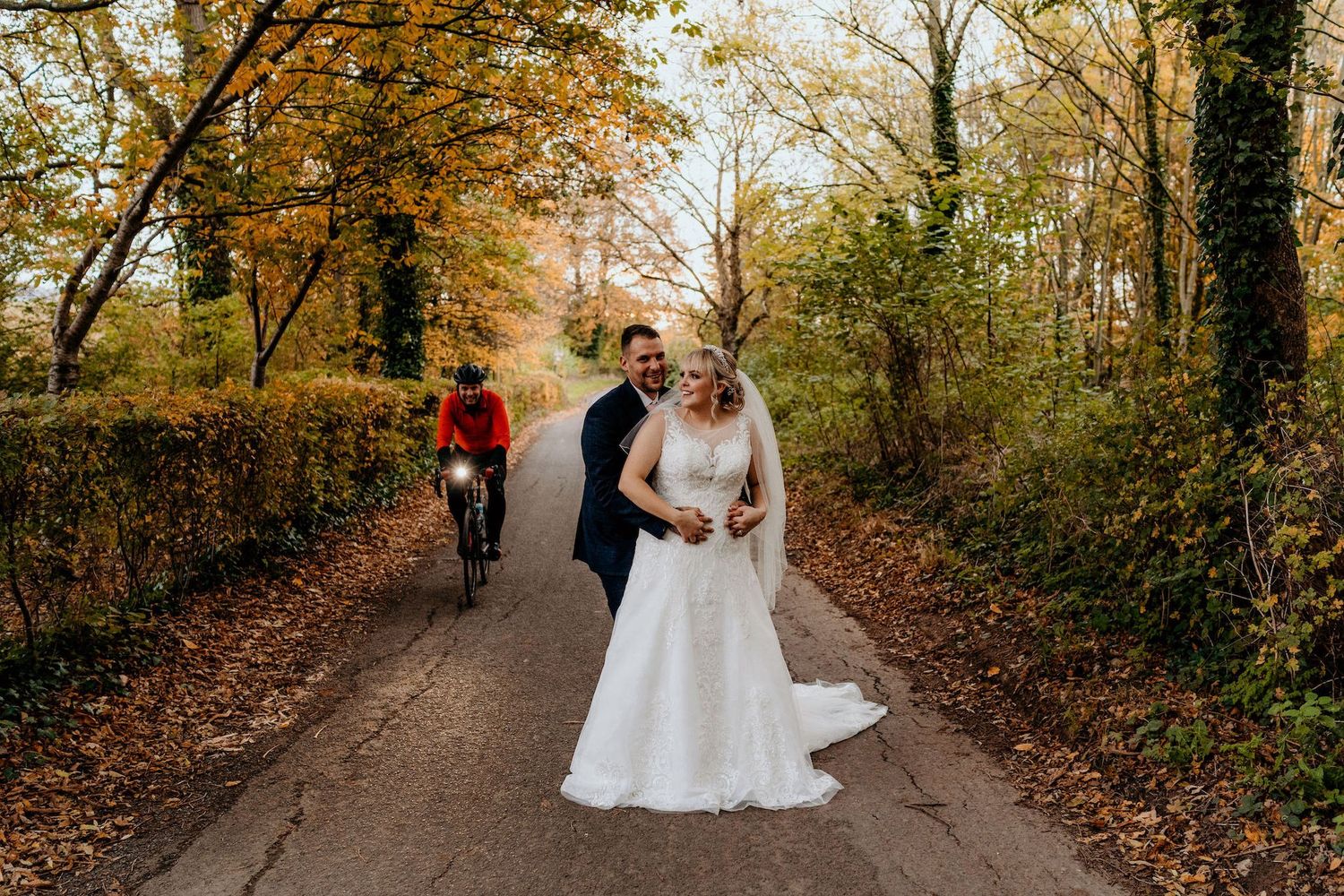 Happy couple walking down a tree-lined autumn path with golden fall foliage overhead.