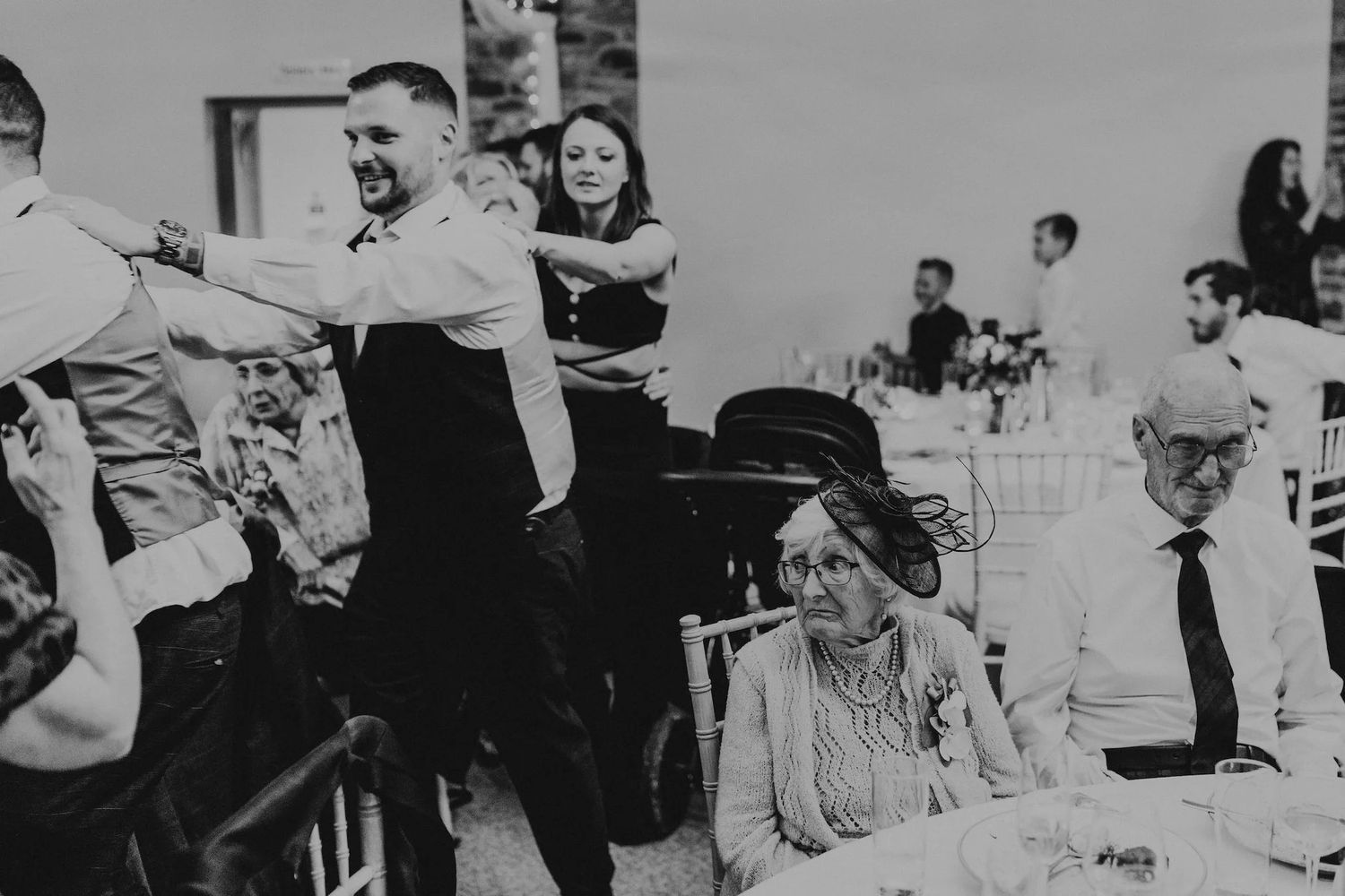 A candid black and white reception photo showing guests enjoying themselves at a wedding celebration.