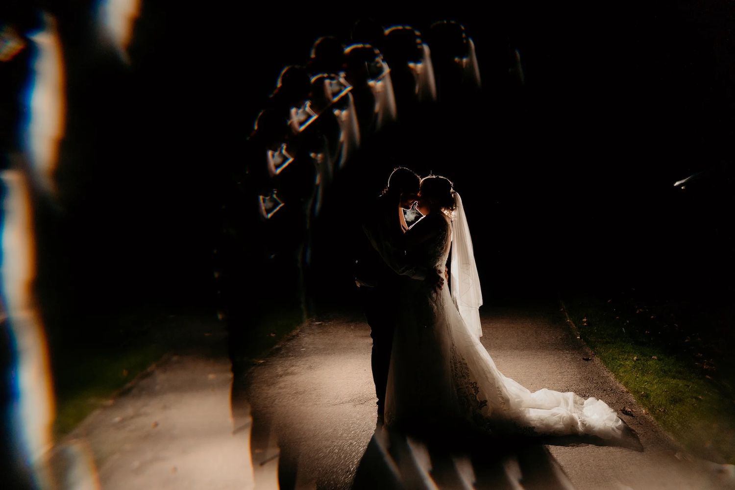 Wedding couple embracing on a dark romantic pathway illuminated by dramatic lighting.