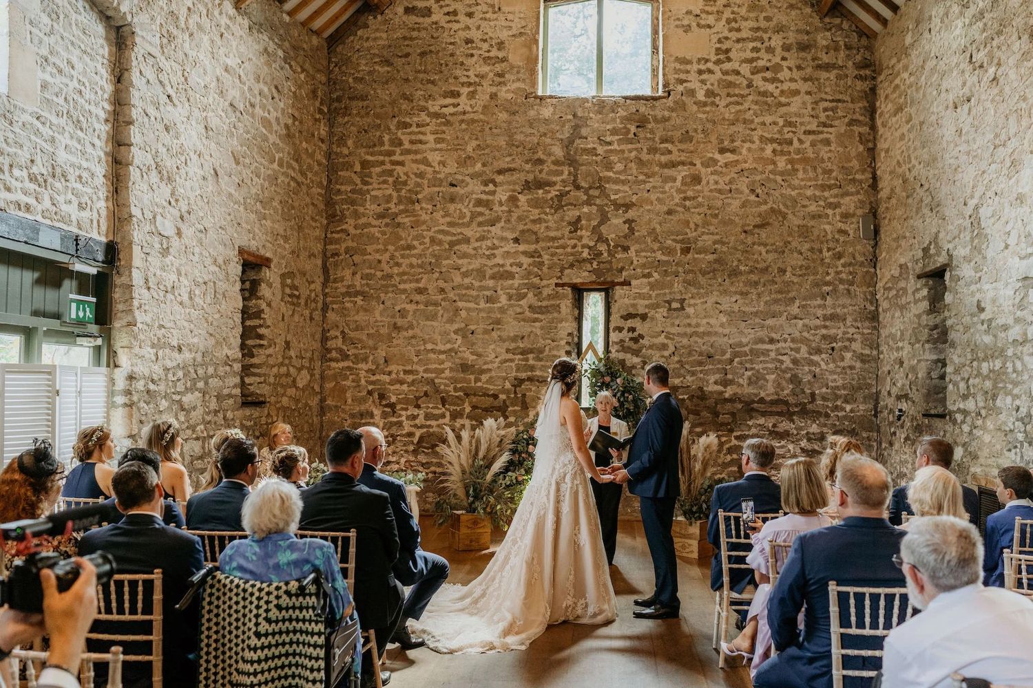 Wedding ceremony setup in rustic brick venue with exposed walls, chairs arranged in rows and floral arrangements.