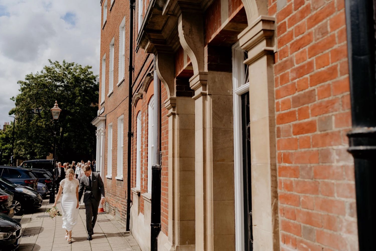 A series of red brick archways and columns line the exterior of an elegant historic building in daylight.