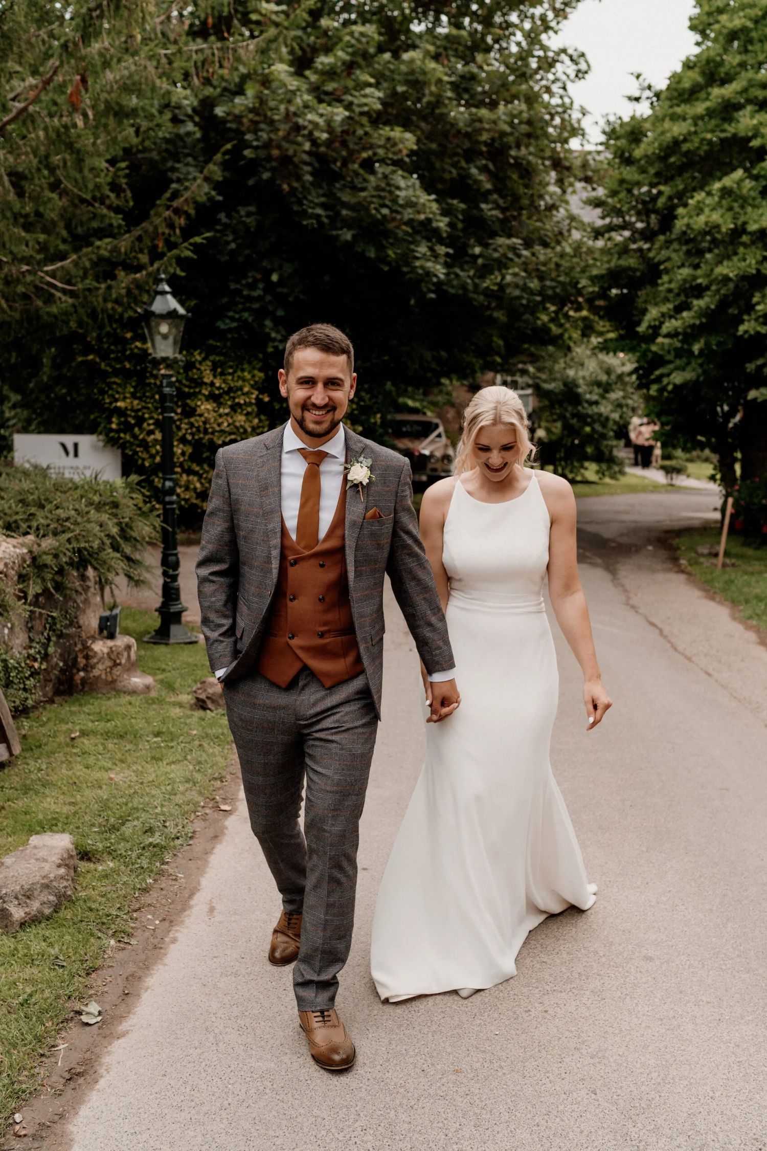 A pair walking hand in hand down a garden path wearing formal wedding attire.