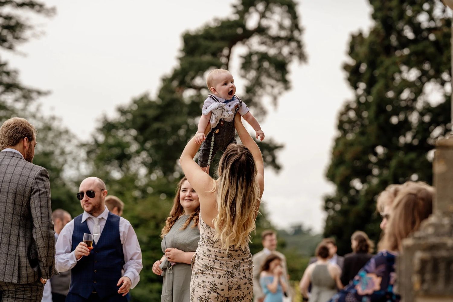 Candid outdoor wedding party celebrations on a sunny day with guests mingling and laughing together.