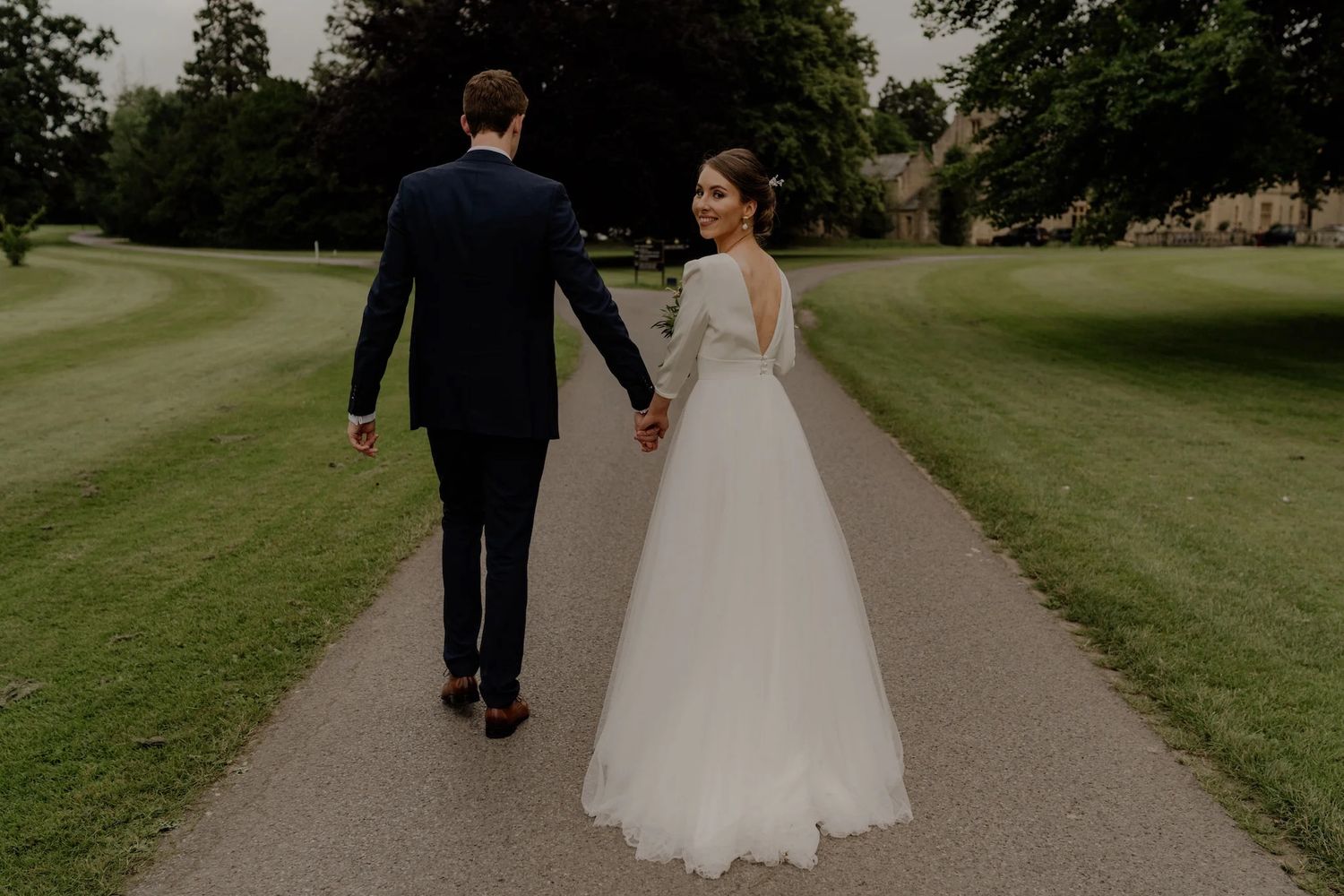 Newlyweds walk hand in hand down a scenic garden path surrounded by lush greenery.