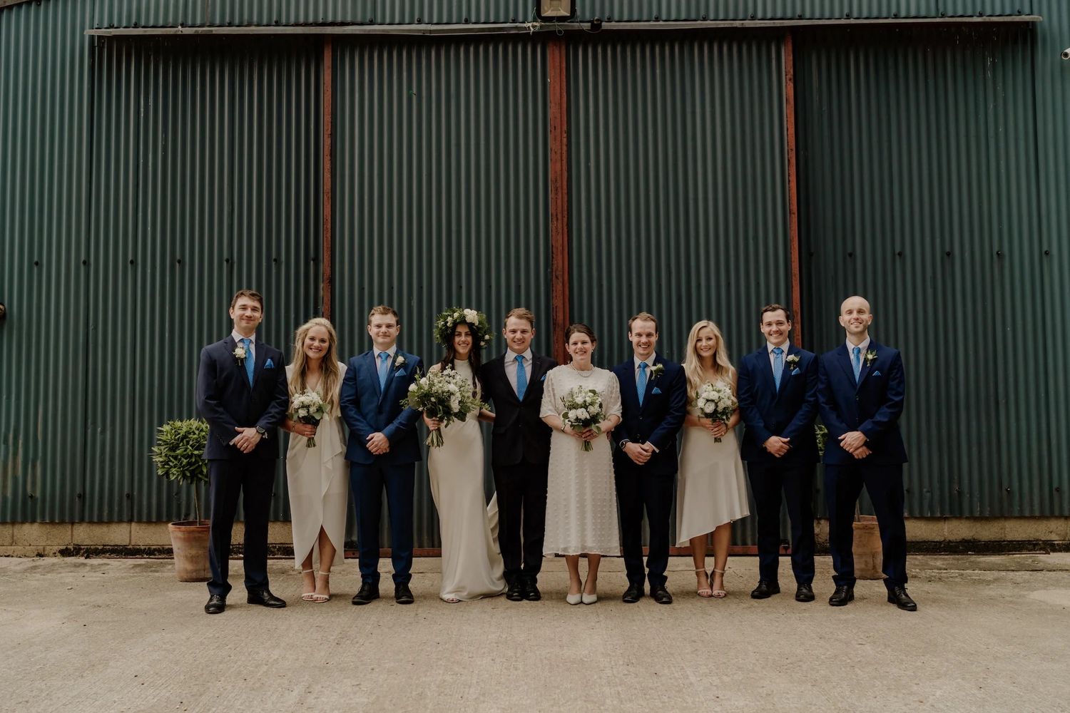 Wedding party poses in front of a green corrugated metal wall for formal portraits.