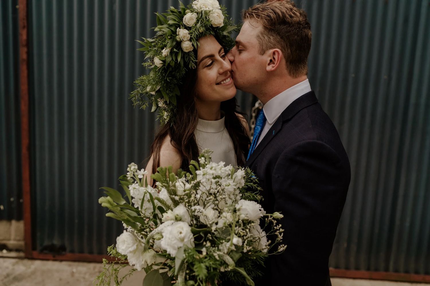 Romantic newlyweds sharing intimate moments in an outdoor garden setting with white floral arrangements.